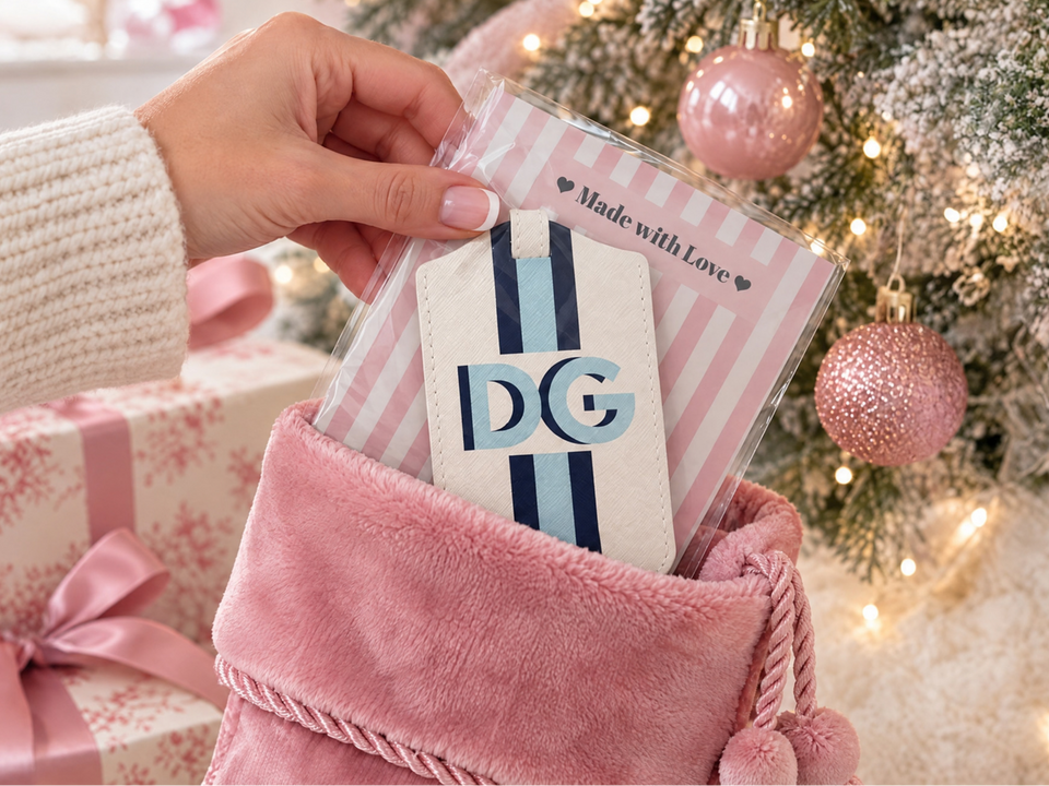 The Stocking Stuffer Edit: personalized luggage tag tucked into a pink Christmas stocking beside holiday gifts and a decorated tree